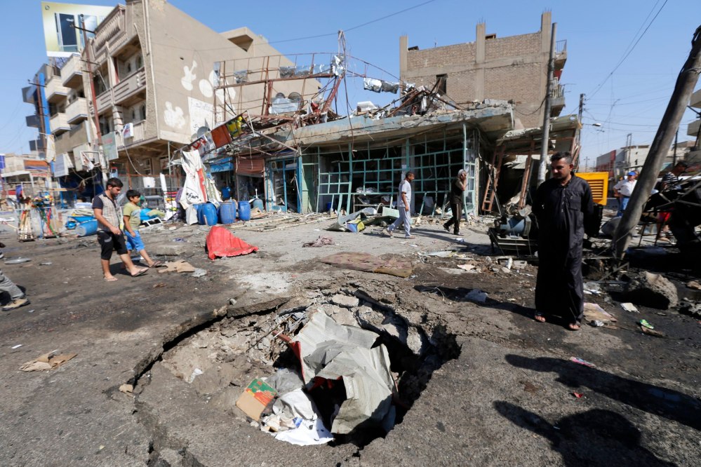 A man looks at the crater caused by an explosion after a car bomb attack in Baghdad's al-Ghadeer district